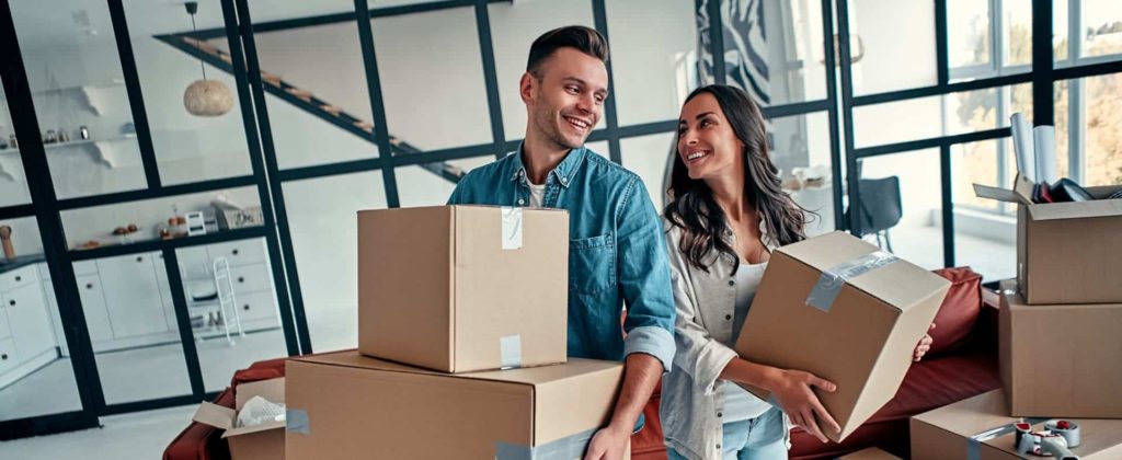 A man and woman, tenants, holding moving boxes in a living room, advanced property management rentals
