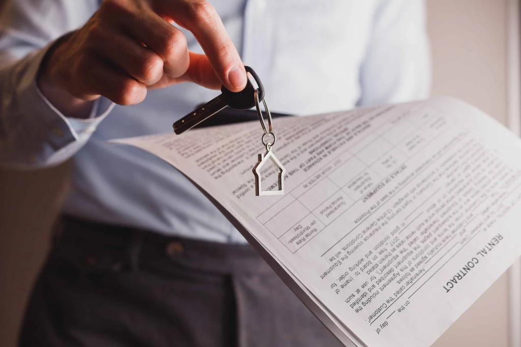 A person holds a set of keys and a rental contract document, ready to meet with property managers.