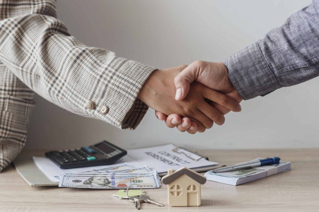 Two people shaking hands in front of a desk, signaling an agreement in property management deal.