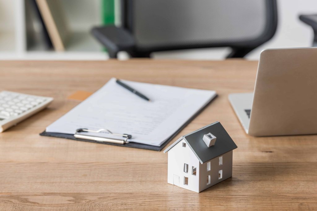 A Property Management Company logo is displayed on a house model placed on a desk next to a laptop.
