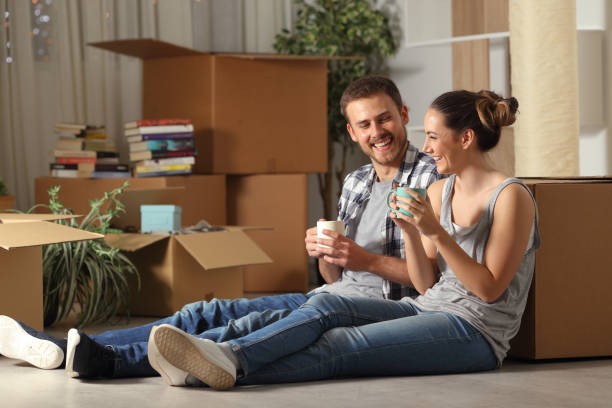 Young couple sitting on the floor in front of moving boxes during their property transition, real property management service