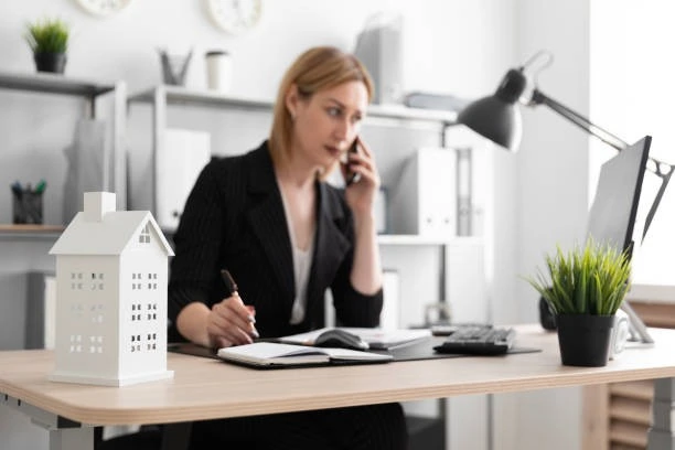 A woman is speaking on the phone while sitting at her desk, possibly discussing real estate or property management services.