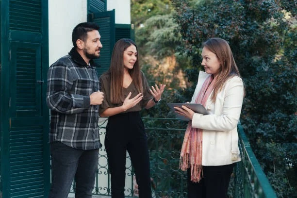 Three people standing on a balcony engage in conversation, while benefiting from real property management services.