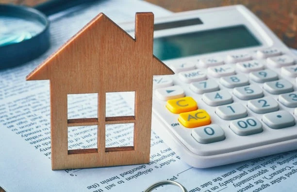 Wooden house model, calculator, and documents on a desk symbolizing property managers' tasks in real estate, finance, or mortgage concept.