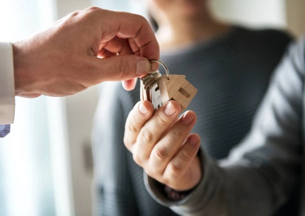 A woman handing a house key to a man, symbolizing dealing with tenants.