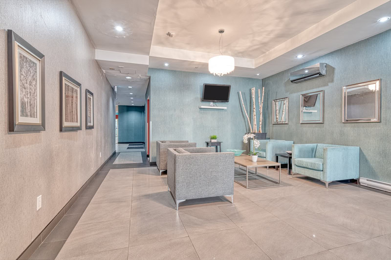 A modern lounge area in our Hamilton rental property features gray and blue seating, elegant wall art, a stunning chandelier, and a flatscreen TV.