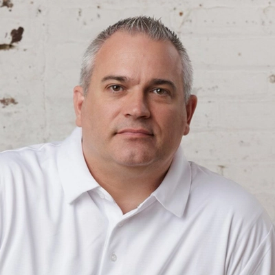 Man in white shirt looking directly at the camera with a slight smile, representing the best property management company, against a textured white brick background.