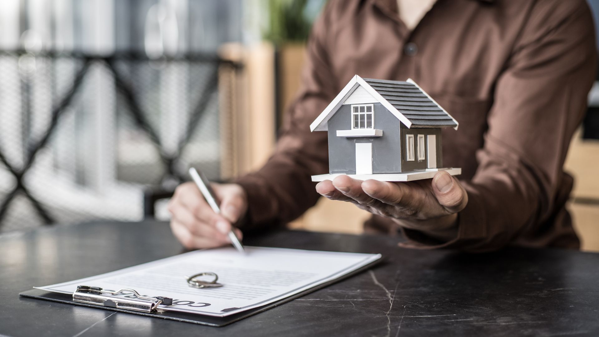 A man signing a contract with a model of a house, symbolizing the future of property management, property management hamilton on