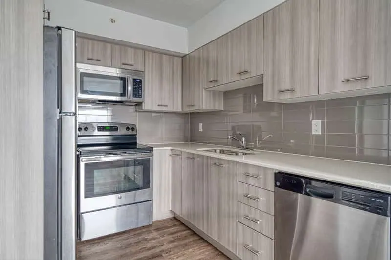 This modern kitchen, ideal for a short-term rental management company, features wooden cabinets and stainless steel appliances, such as a fridge, oven, microwave, and dishwasher, complemented by a stylish tiled backsplash.