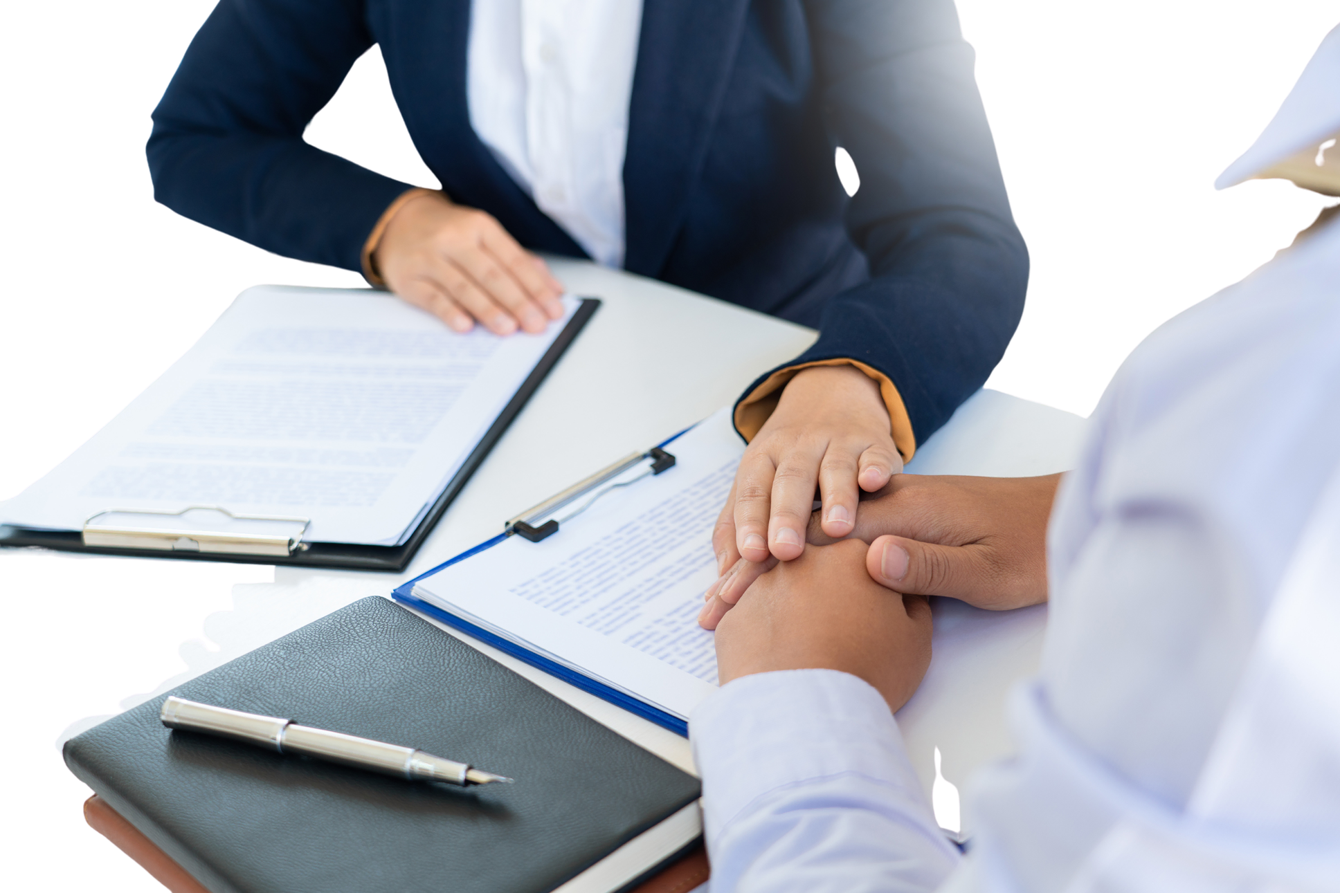 Two people are seated at a table with documents, a clipboard, and a pen. One person is holding the other's hand in a gesture of support or reassurance, highlighting the compassionate side of legal services.