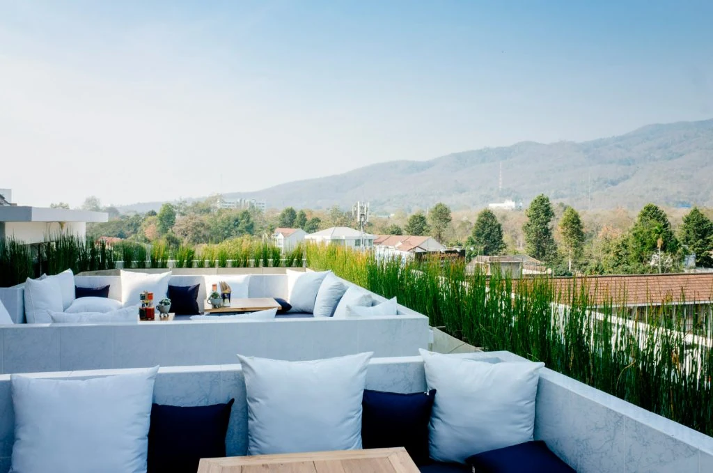 Rooftop terrace with white seating and cushions, a table with beverages, overlooking a scenic view of trees and mountains under a clear sky—one of the standout apartment amenities.