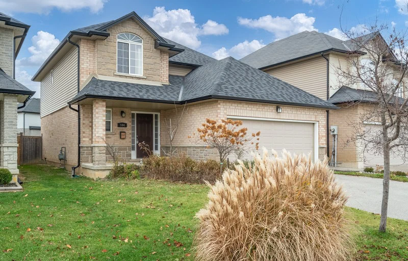 A two-story brick house with a gable roof, a two-car garage, and a front lawn featuring a small tree and ornamental grass sits in an area reflecting the latest rental market trends in Hamilton.