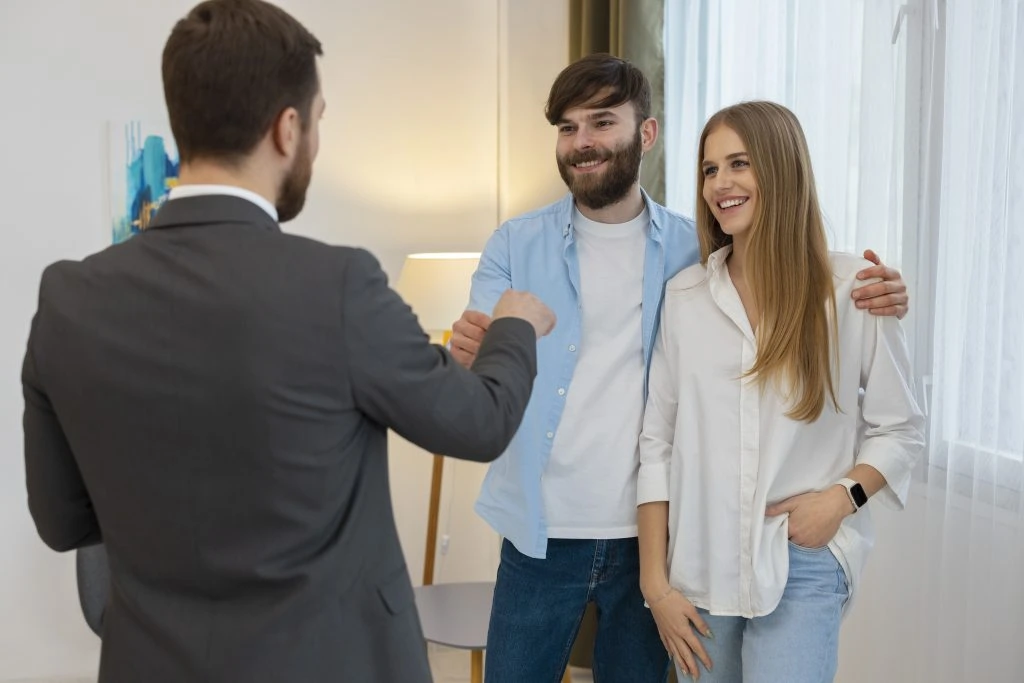 In a bright room, a man in a suit fist-bumps a casually dressed man, while a woman smiles beside them—perhaps they've just closed a deal with one of the top property management companies in Hamilton.