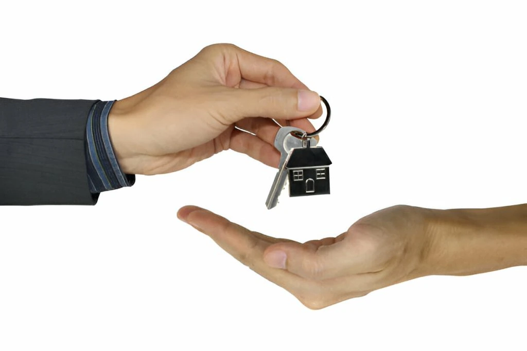 A hand is handing over a keychain with a house-shaped charm and key to another open hand, symbolizing effective marketing strategies to attract new tenants.