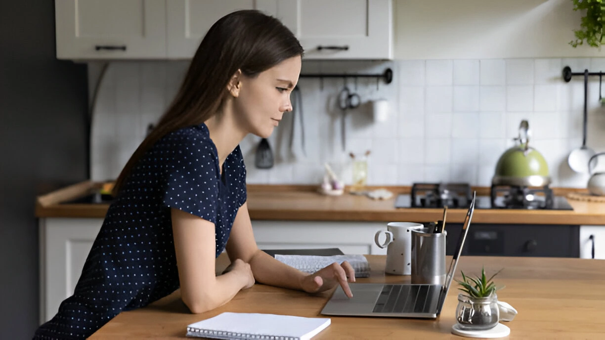 A woman is sitting at a table using a laptop, diligently working on tenant screening, residential property management services