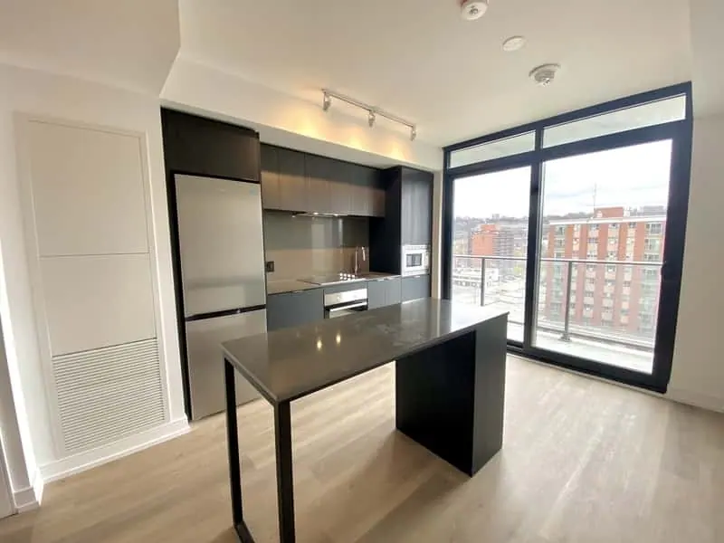 A modern kitchen with black cabinets, stainless steel appliances, an island with a dark countertop, and large windows overlooking a cityscape is ideal for those seeking efficient property management services near me.