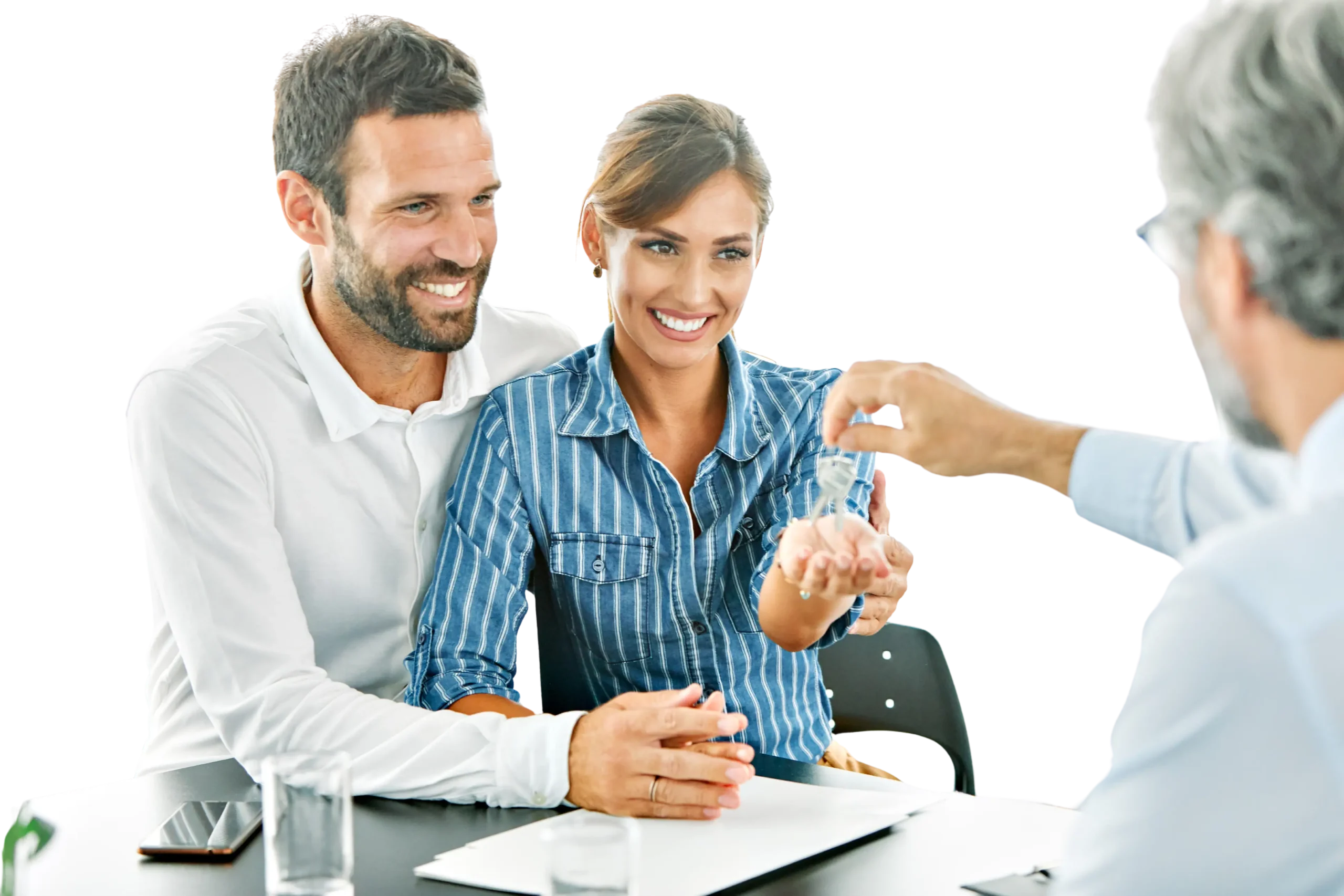 A couple, smiling, receives a key from a person sitting across the table in a business setting, their expressions reflecting the optimism of using an investment calculator for their future plans.