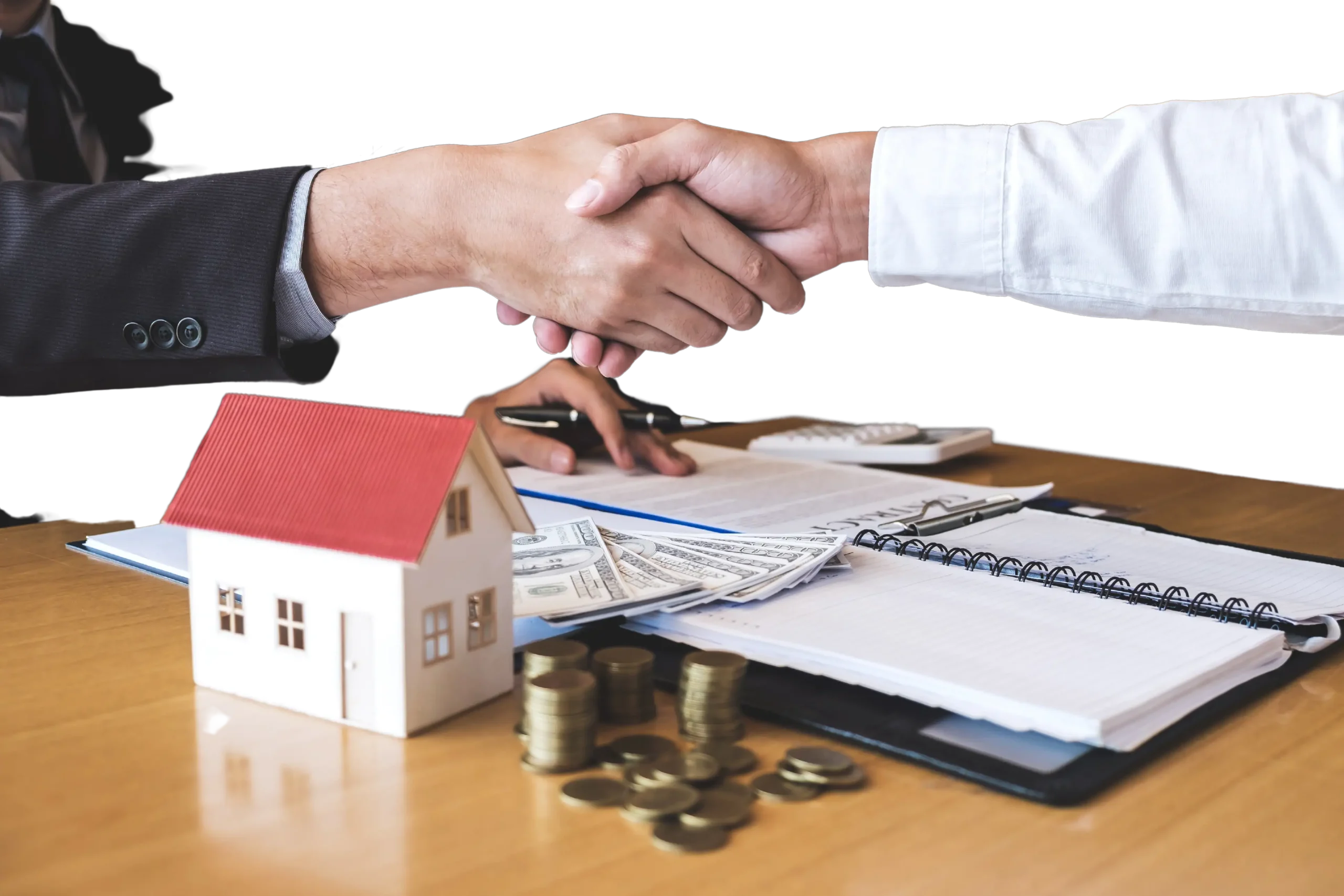 Two people shaking hands over a desk with a small house model, stacks of coins, dollar bills, an investment calculator, and paperwork.