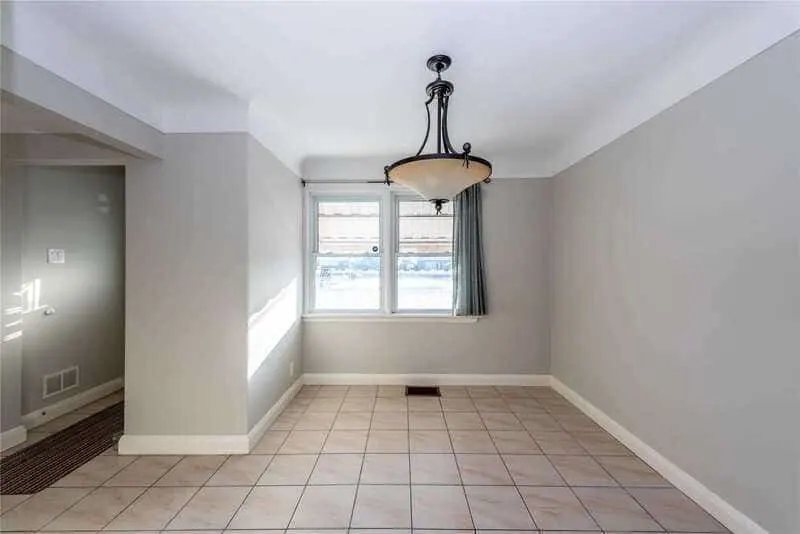 Empty room with tiled floor, a large window with a curtain, a hanging light fixture, and light gray walls, maintained by a good property management company.