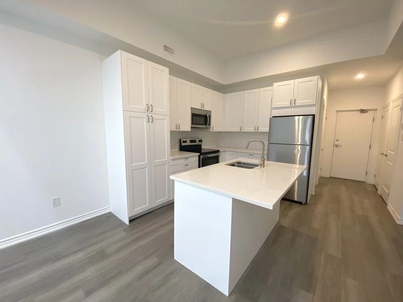 A modern kitchen with white cabinets, stainless steel appliances, a center island with a sink, and a light grey floor showcases the touch of a good property management company.