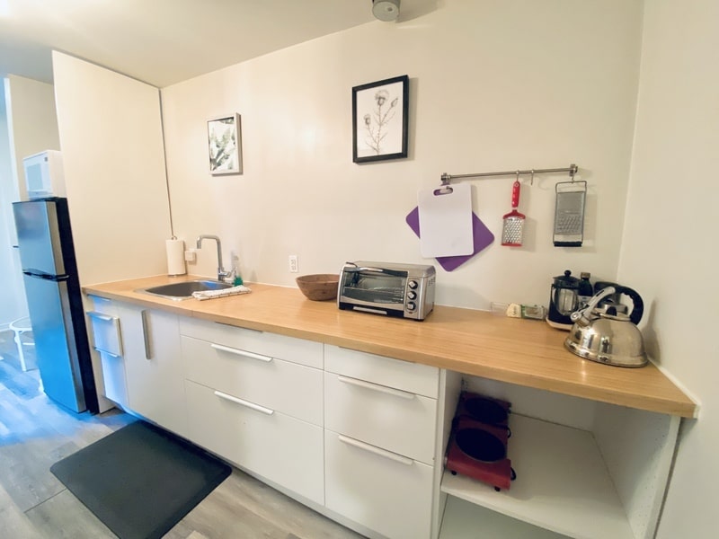 A modern kitchen with white cabinets, a wooden countertop, a sink, a small oven, a tea kettle, and various kitchen utensils. A black refrigerator and wall art are also visible—reflecting the standards set by a good property management company.