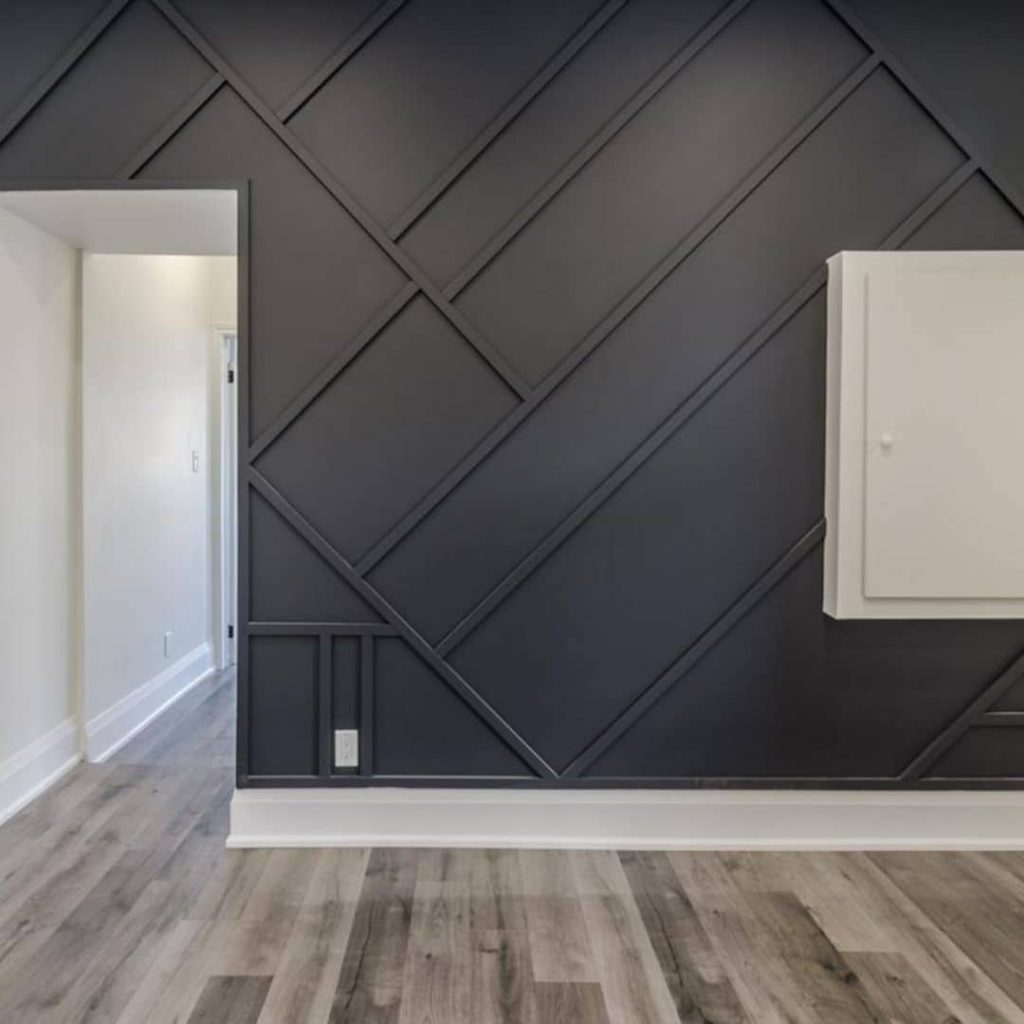 The interior view showcases a room with a dark accent wall featuring a geometric pattern, complemented by light wood flooring. A doorway leads to an adjacent space, perfect for clients of our rent management company seeking stylish and functional living spaces.