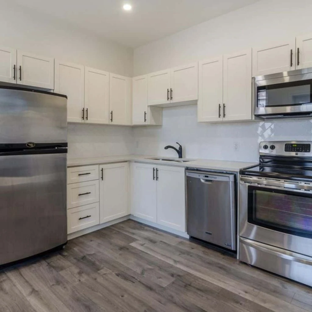 A modern kitchen with stainless steel appliances, white cabinets, and wood flooring is managed by a leading rent management company. It features a refrigerator, oven, microwave, dishwasher, and sleek black faucet.