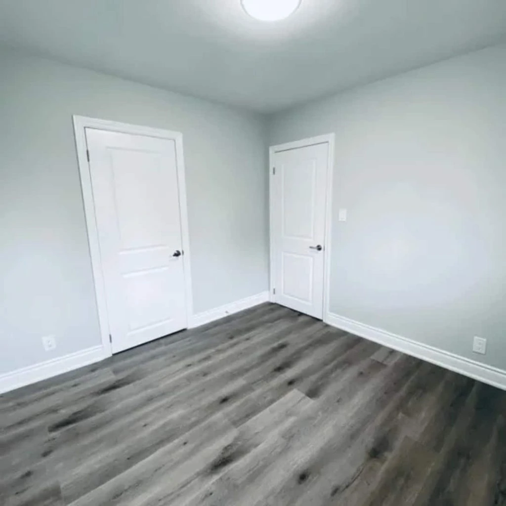 An empty room with light gray walls, a dark wood floor, and two white doors offers a blank canvas, making it ideal for property management agencies to envision endless possibilities.