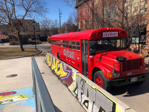 A bright red City Kidz bus is parked on a street beside colorful graffiti-covered barriers on a sunny day.