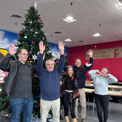 Five people stand smiling with raised hands in front of a beautifully decorated Christmas tree, adding festive cheer to the indoor setting. This joyful scene is a testament to why they are part of the best property management company Hamilton has to offer.