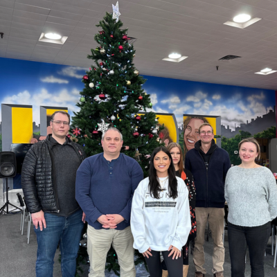 Six people stand together indoors, in front of a beautifully decorated Christmas tree, embodying the warmth and unity that make gatherings memorable. This could be a festive highlight for any property managed by the best property management company in Hamilton.