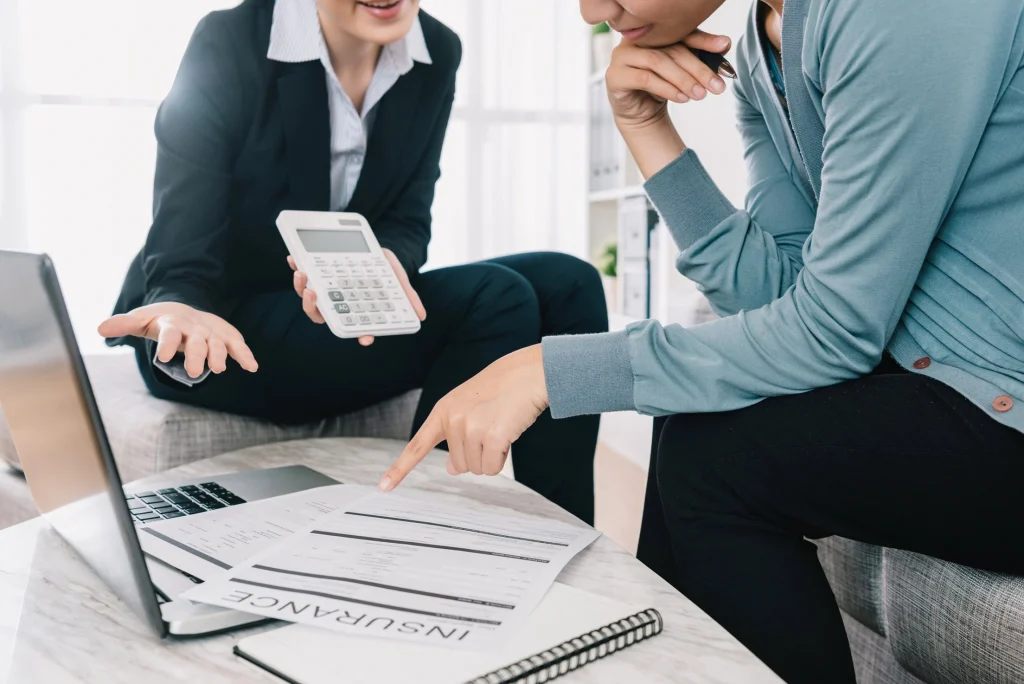 Two people are engaged in a discussion about insurance documents at a table equipped with a laptop, notepad, and calculator. One points to the document while the other holds the calculator, reflecting on property management services in Hamilton.