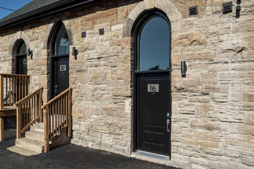 Exterior view of a stone building featuring two black arched doors, numbered 116 and 117, enhanced by wooden stairs leading to the door on the left—a prime example of advanced property management in Hamilton's rental scene.