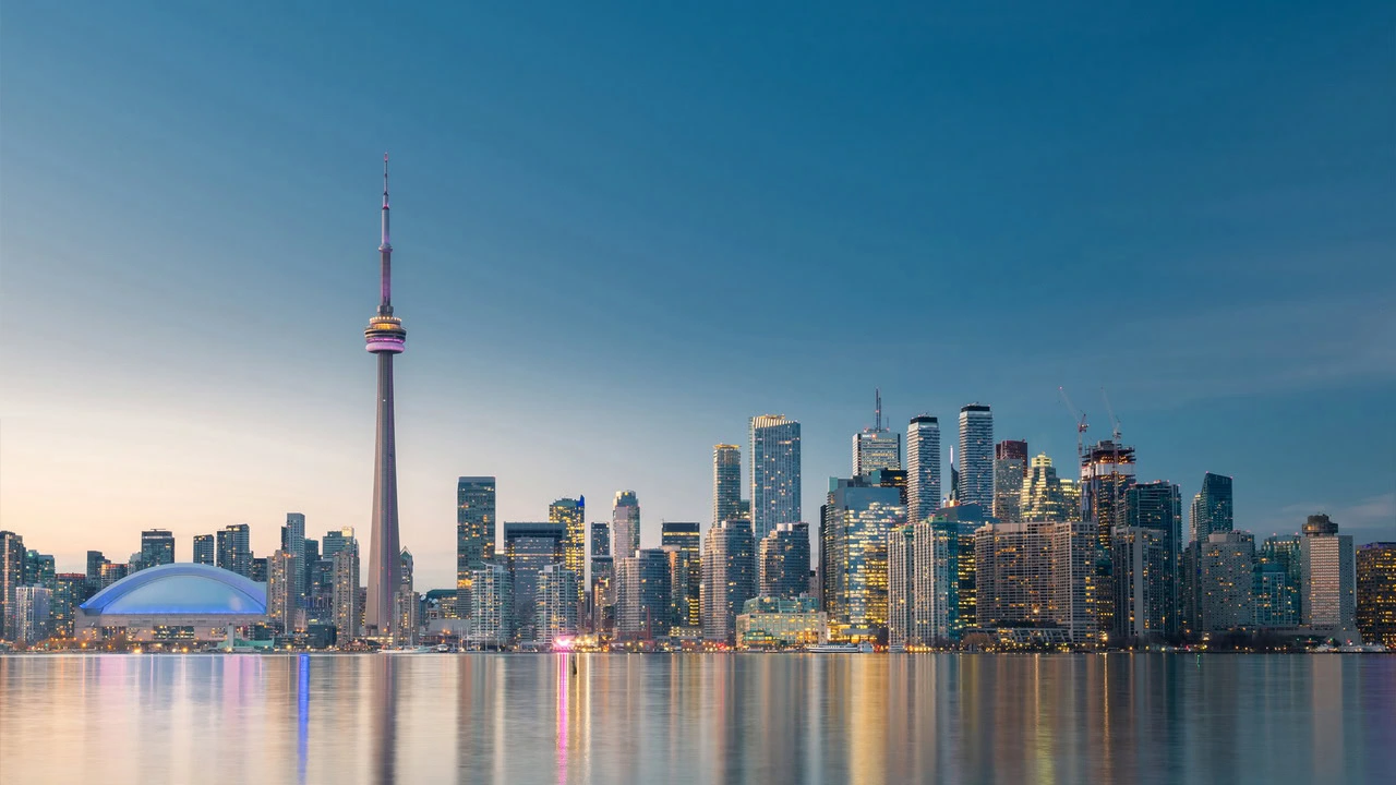 The skyline of a city, dominated by the LTB-Forms tower, is beautifully reflected in a tranquil body of water at dusk, with various buildings adding to the serene vista.