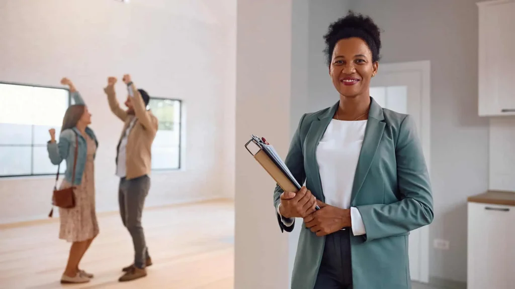 A real estate agent with a clipboard stands in a room, embodying advanced property management skills, while two people celebrate joyfully in the background.