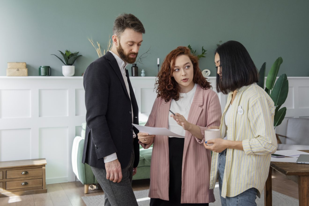 Three people stand together in an office, discussing Ontario LTB Forms; one woman gestures while holding papers, and the others listen attentively.