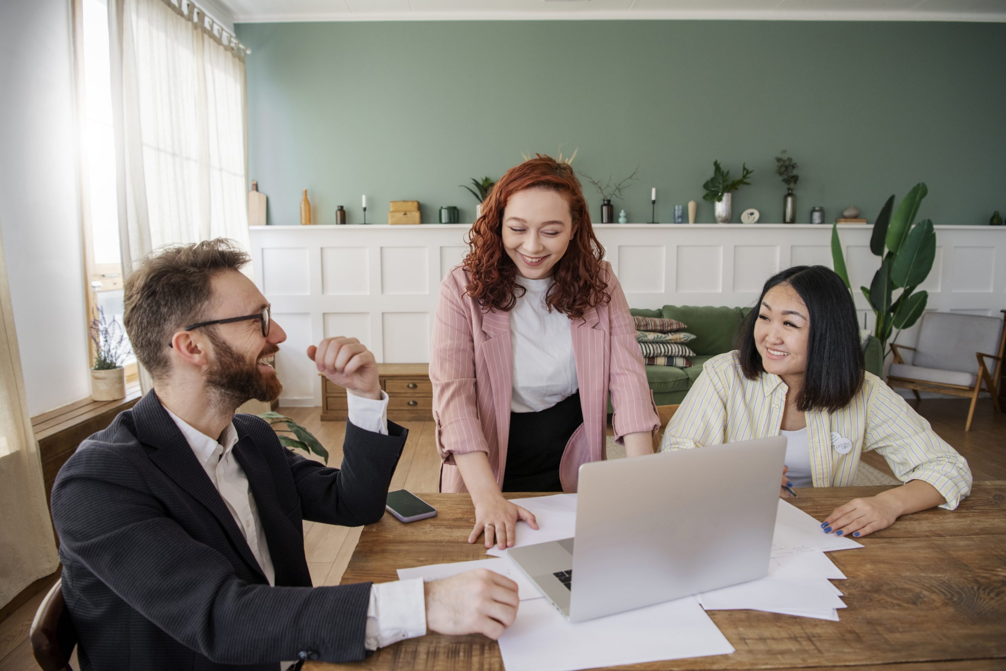 Three colleagues are gathered around a table with a laptop and papers, engaged in a discussion about Property Management in Hamilton in a well-lit office.