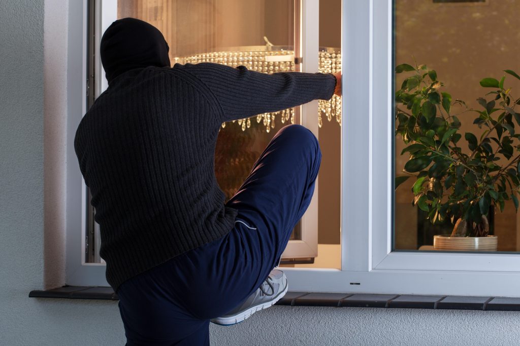 man black sweater blue pants is trying get into window with white light hanging from it